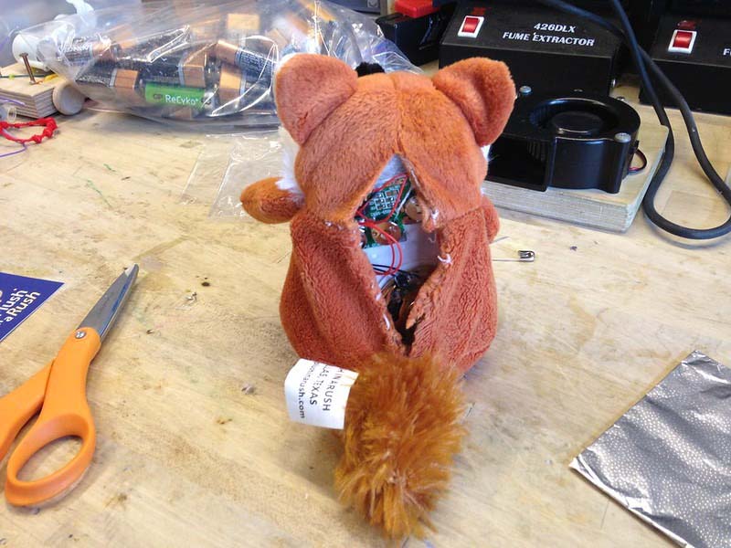 Stuffed animal opened at the back on a workbench, revealing internal electronic components and wiring during repair or inspection