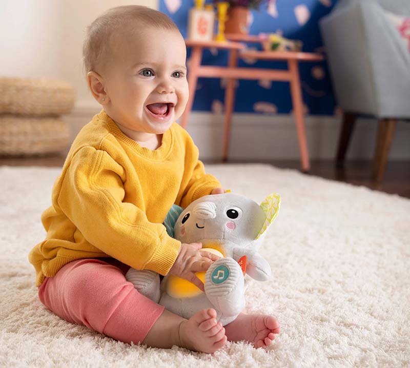 Smiling baby sitting on carpet playing with a soft interactive plush toy