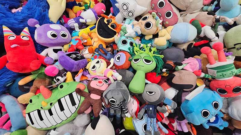 Large pile of colorful plush toys with cartoon-style faces and varied shapes, tightly packed together to create a vibrant and playful assortment of stuffed animals.