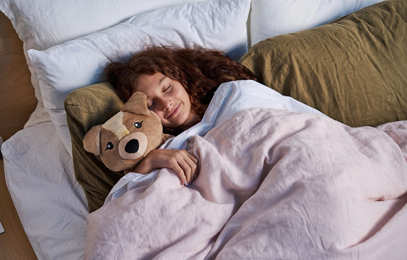 Girl sleeping peacefully while cuddling a weighted stuffed animal under a blanket