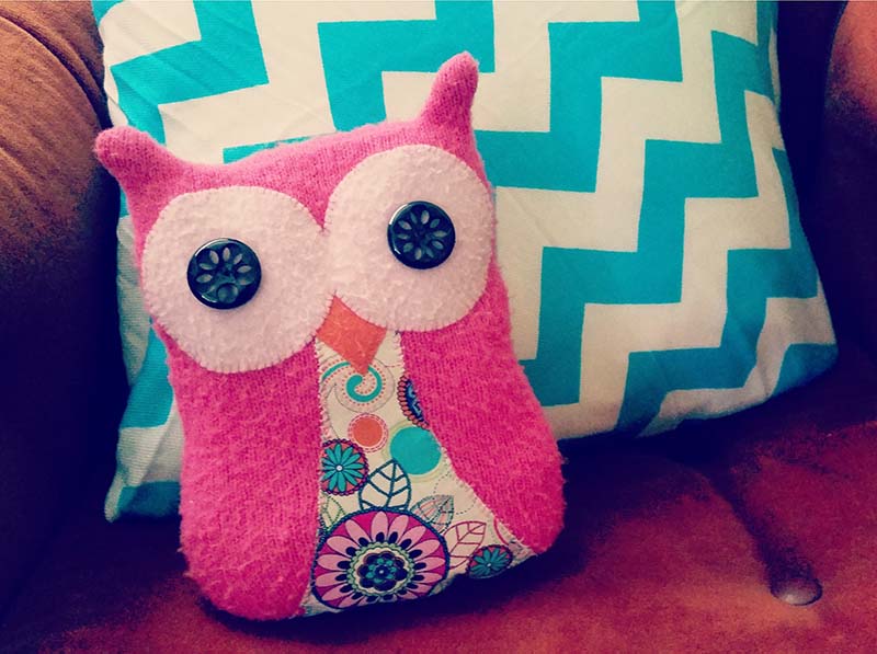 Pink owl plush pillow with patterned fabric, resting on a couch