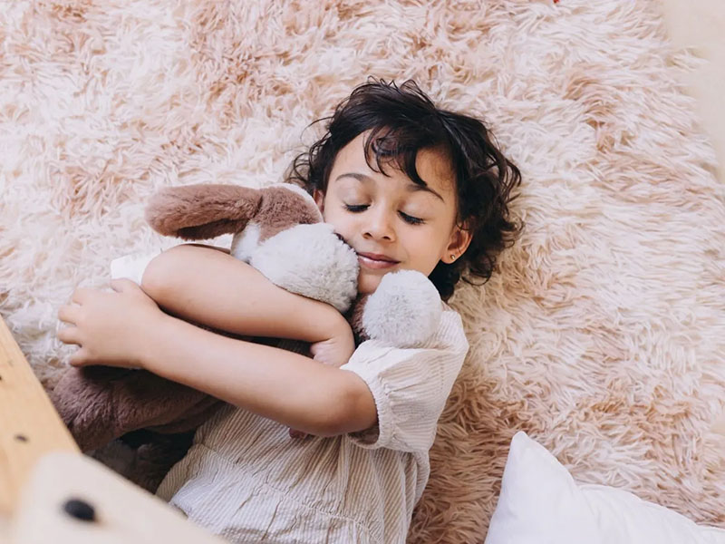 Child hugging a soft plush toy while resting on a fluffy rug