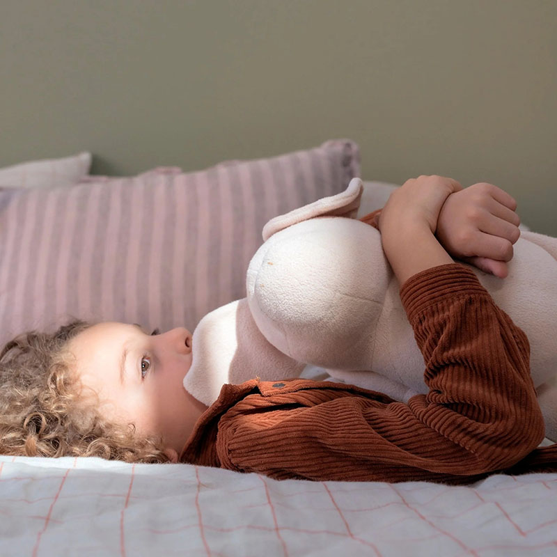Baby lying in bed cuddling a soft plush toy close to face