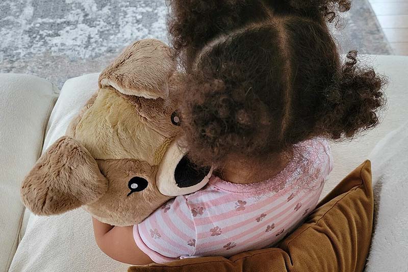 A young child sitting on a couch, hugging a soft dog plush toy close for comfort and security