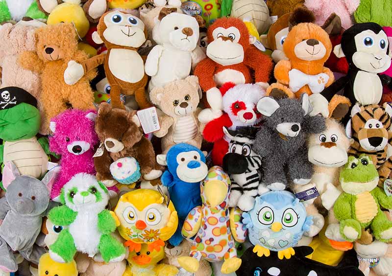 Colorful assortment of stuffed animals and plush toys tightly packed together, including bears, monkeys, owls, and other animals