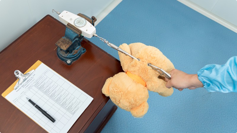 A plush toy is tested for pull strength to ensure secure seams and attachment safety.