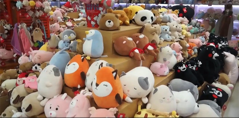 Large retail display filled with assorted plush toys, including bears, cats, penguins, and cartoon-style stuffed animals arranged on tiered shelves