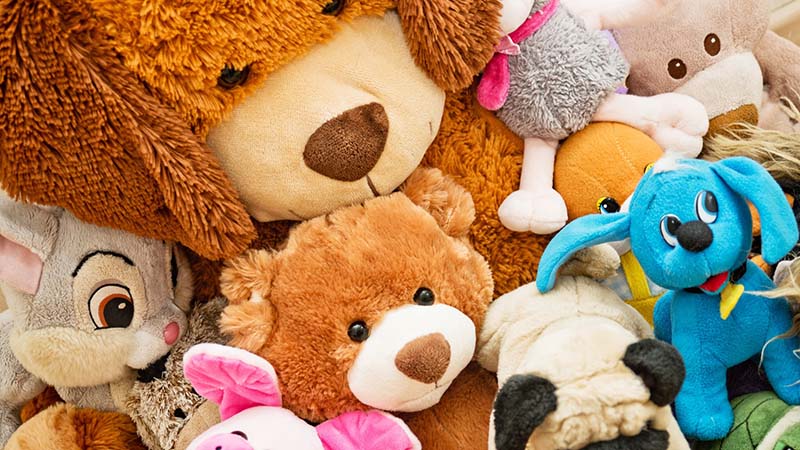 Close-up of assorted plush stuffed animals, including teddy bears and colorful character toys packed together.