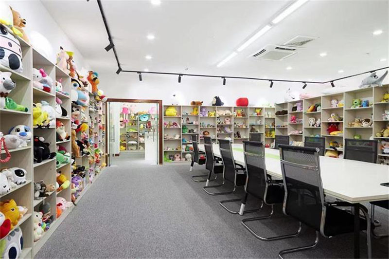 Bright showroom meeting room with shelves full of plush toy samples along the walls and a long conference table with chairs.