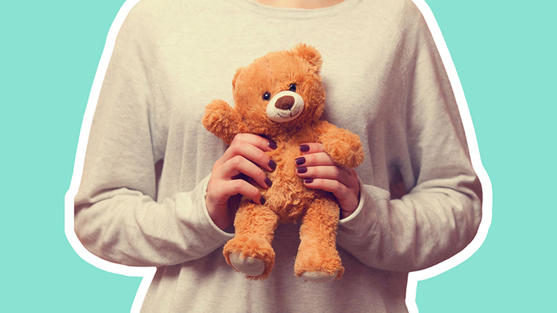 Person holding a small brown teddy bear with both hands against a light teal background