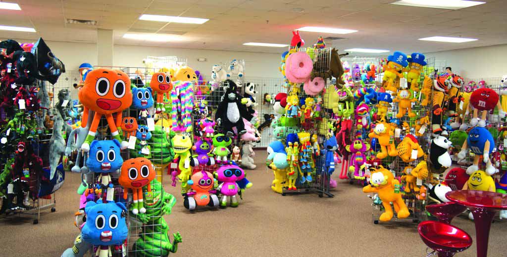 Large indoor showroom filled with colorful plush toys and character dolls displayed on racks and grid panels under bright ceiling lights.