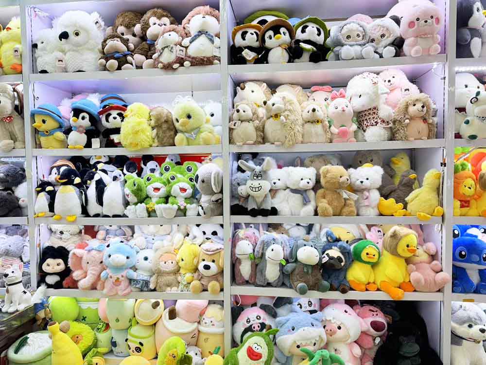 Shelves filled with assorted plush toys, including penguins, bears, rabbits, ducks, and character stuffed animals in a showroom.
