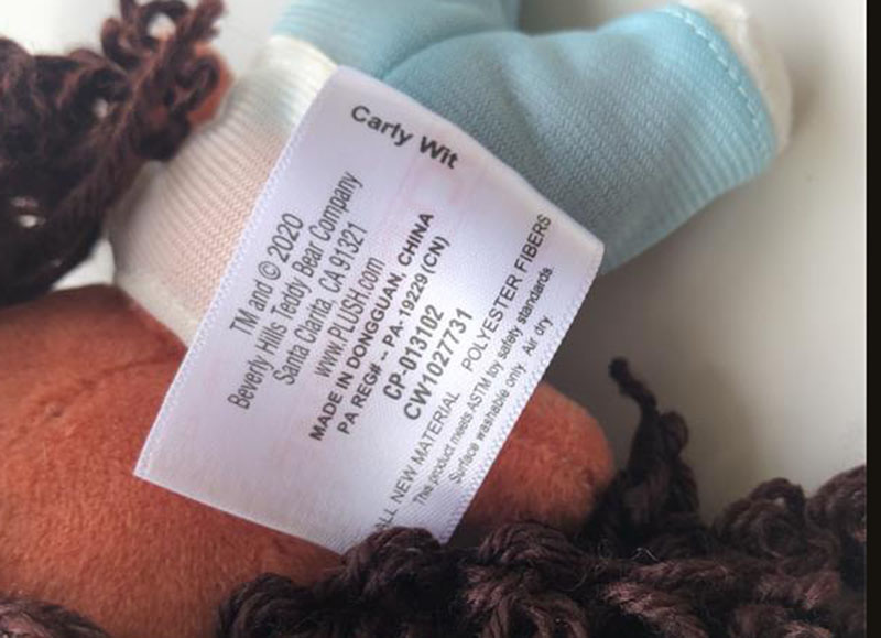 Close-up of a plush toy fabric care label showing manufacturer details, materials, and “Made in China” information.