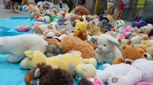 A large collection of stuffed animals spread across a blue tarp outdoors, with many plush toys piled together in a public street setting.