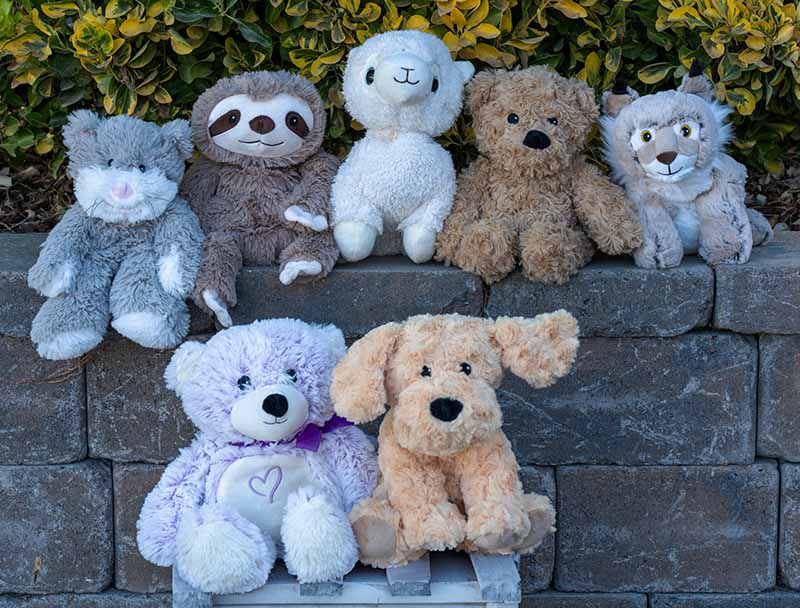A group of plush stuffed animals arranged on stone steps outdoors, including cat, sloth, lamb, bear, wolf, teddy bear, and dog