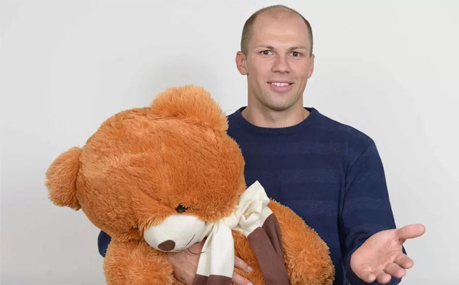 Man presenting a large plush teddy bear, emphasizing size and soft texture.