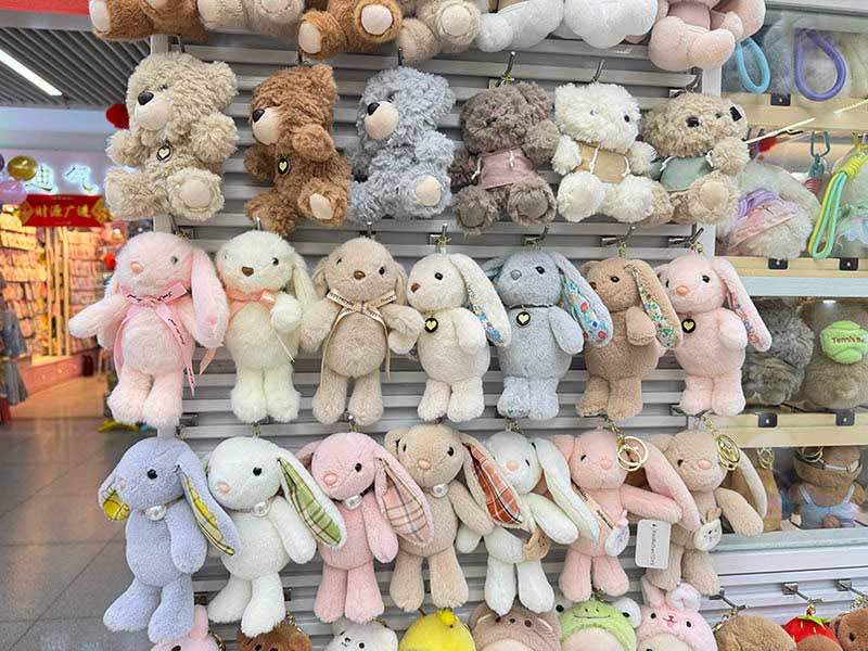 A variety of plush toys displayed on hooks, showcasing different styles, colors, and retail-ready designs.