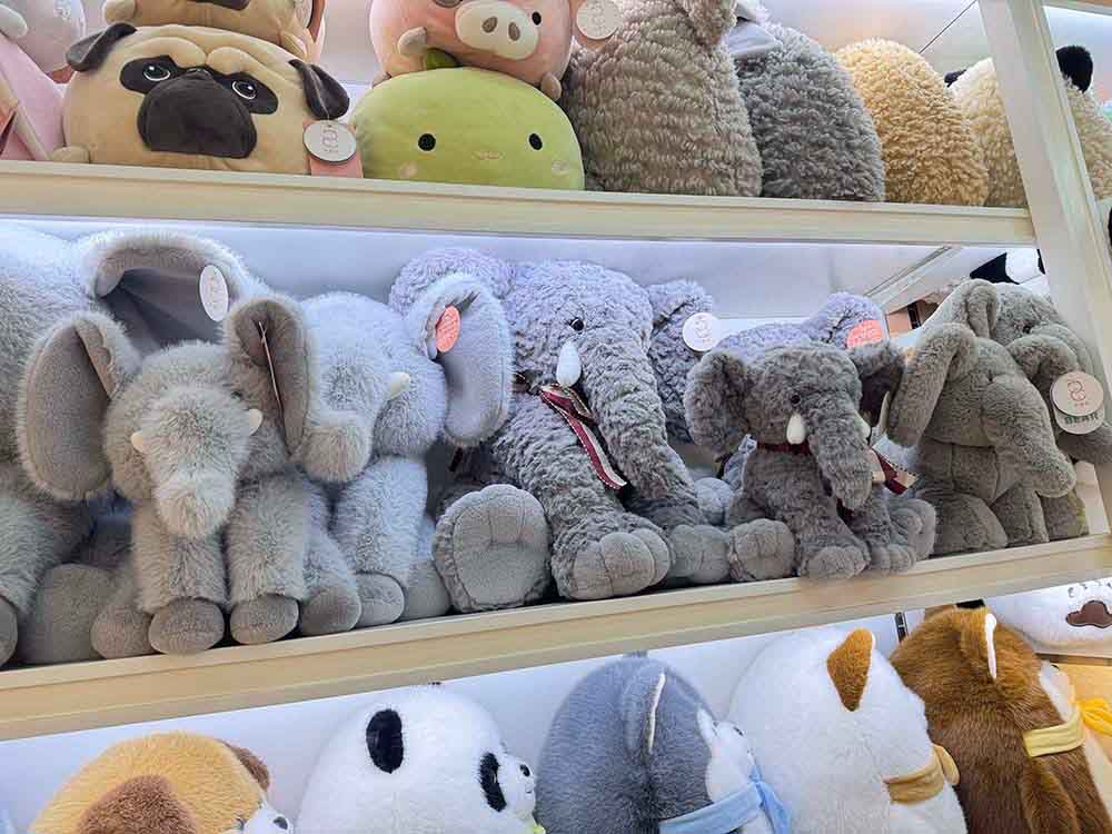 Soft elephant plush toys displayed in various sizes and shades, arranged neatly for retail presentation.