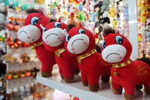 Bright red horse plush toys lined up on a retail shelf, featuring embroidered details and decorative gold collars.