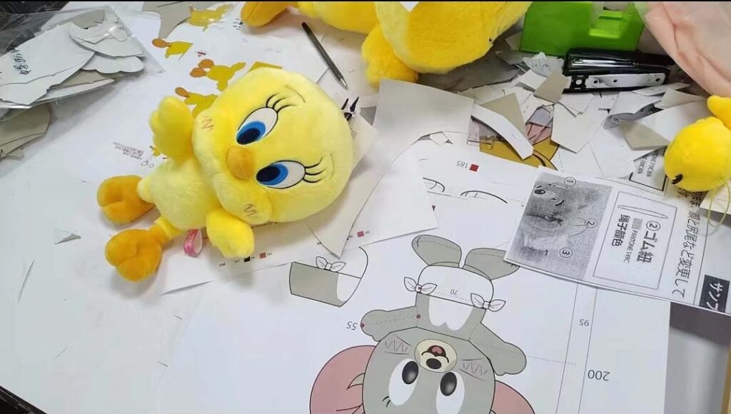 A plush toy sample placed alongside pattern drawings and cut pieces during the development and prototyping stage.