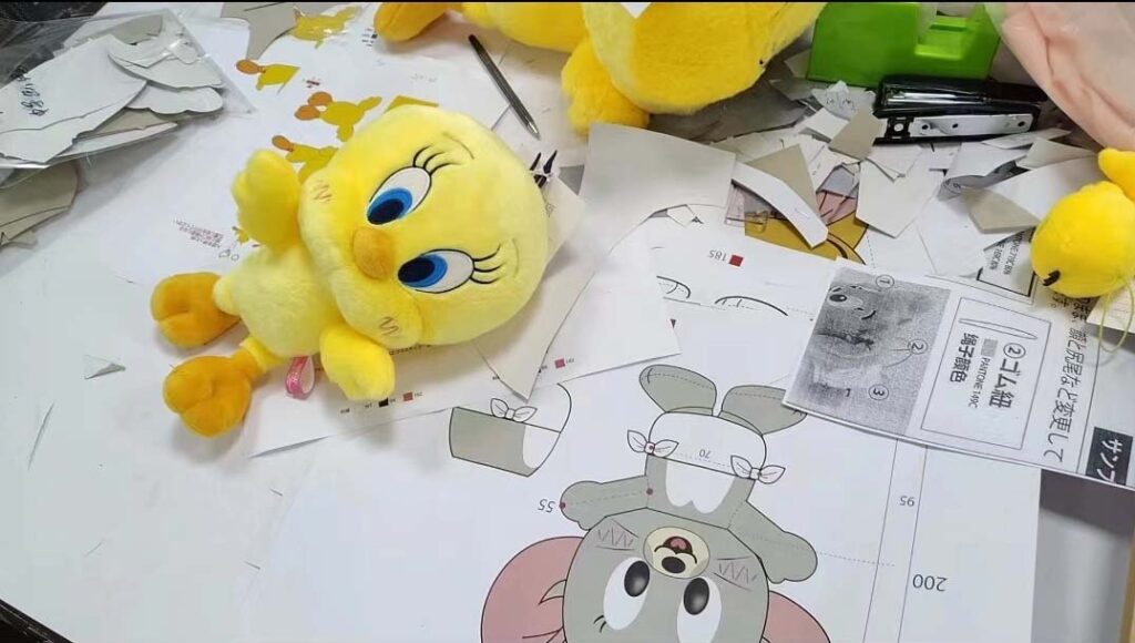A plush toy prototype and paper patterns displayed on a worktable, showing the early design and pattern-making stage in plush toy development.