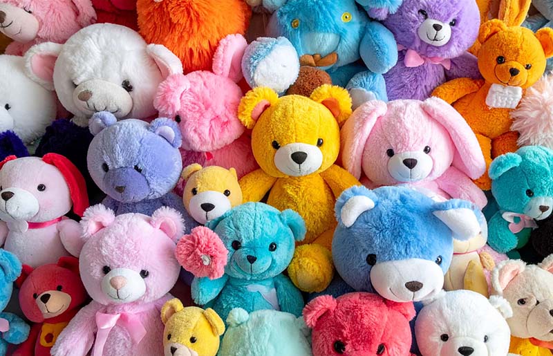 A vibrant assortment of teddy bear plush toys in various bright colors and sizes, displayed together to showcase product variety and mass production capability.