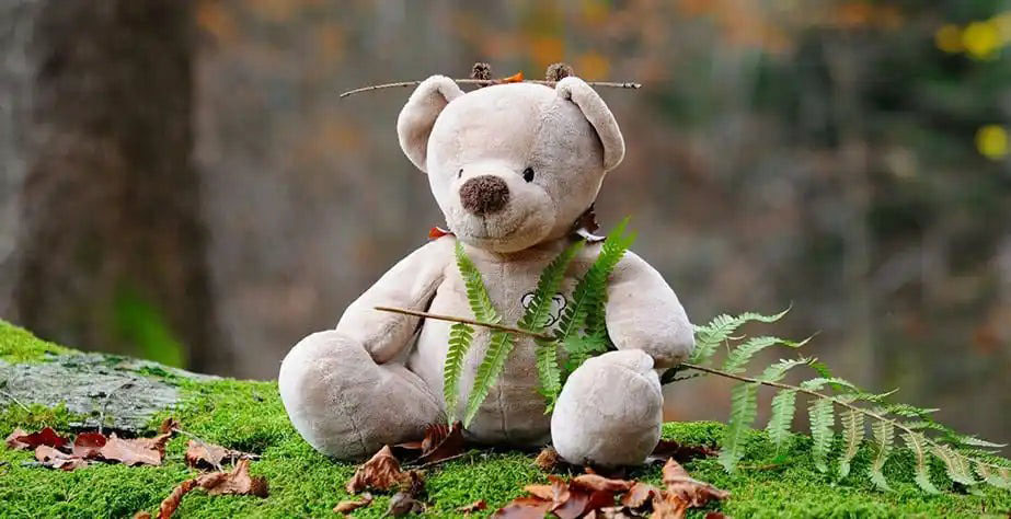 A soft teddy bear plush toy sitting outdoors on moss and leaves, creating a warm and cozy scene that highlights the classic comfort of plush toys.