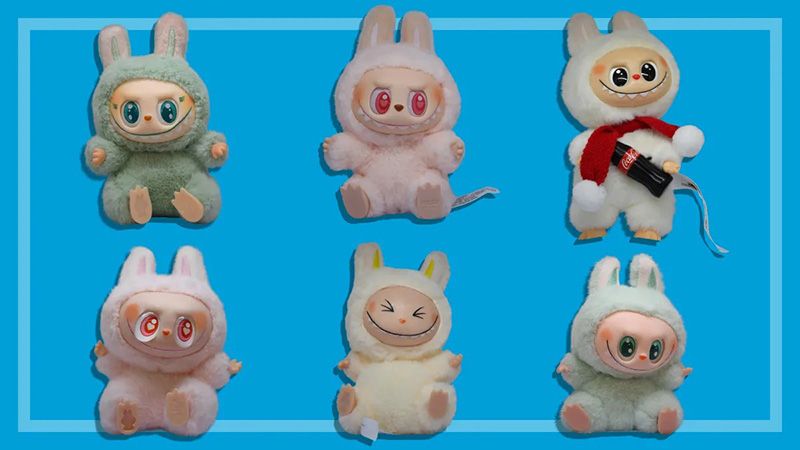 A lineup of character plush dolls displayed against a blue background, showcasing different color variations, facial expressions, and themed accessories within the same product series.
