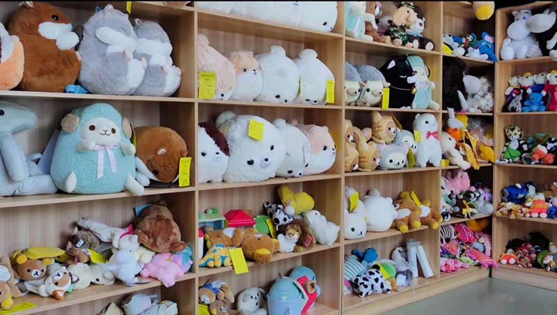 Shelves filled with various plush toy samples in different shapes, sizes, and styles, showcasing design diversity and development capabilities in a manufacturer’s sample room.