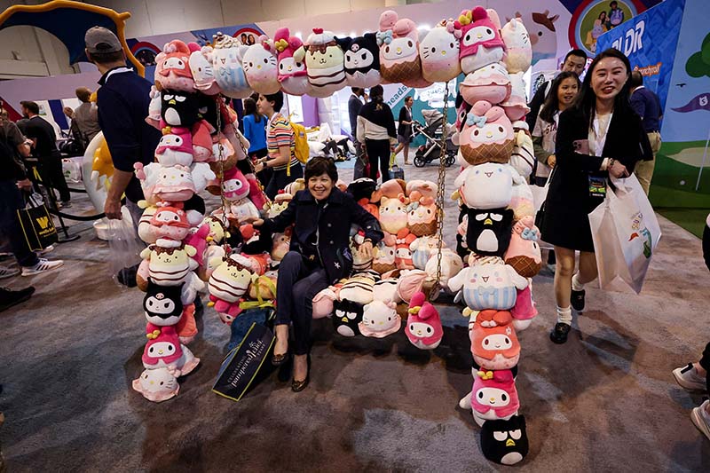 Visitors posing with a large display made of colorful character plush toys at a toy exhibition booth, highlighting brand promotion and fan interaction.