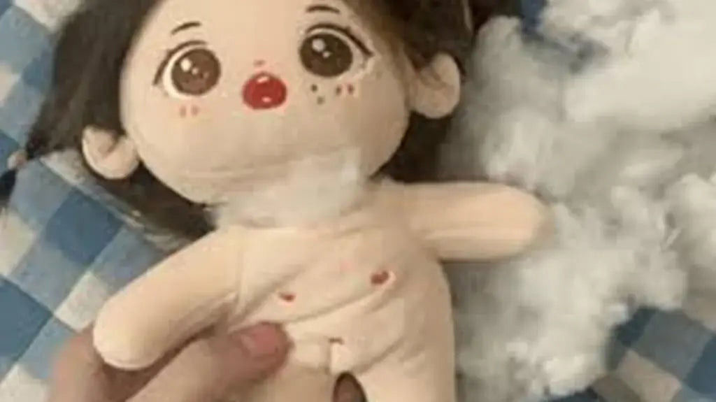 A soft cloth doll shell is shown before stuffing, featuring a printed cartoon-style face with large eyes, rosy cheeks, and dark hair. The image highlights the semi-finished stage of doll production, showing the outer fabric body before filling and final assembly.
