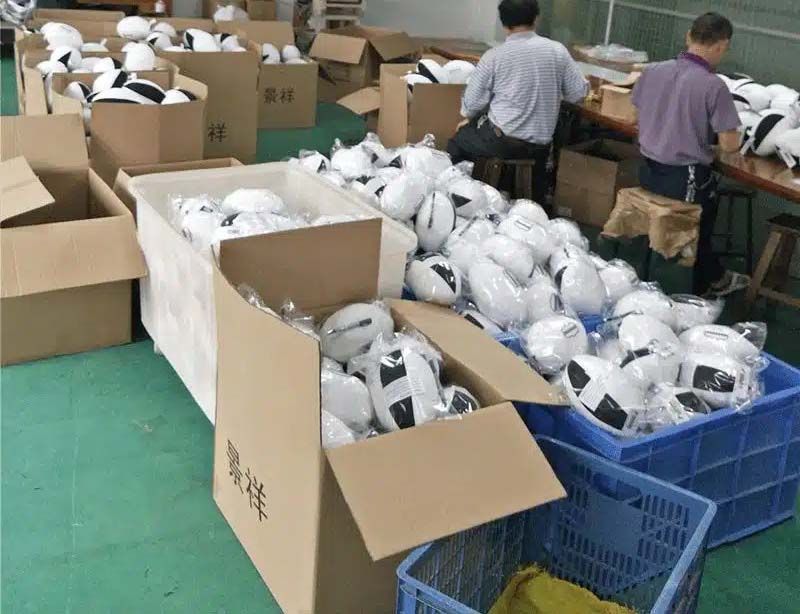 Workers packing finished plush toys into cartons and plastic bags in a factory setting, preparing bulk orders for shipment.