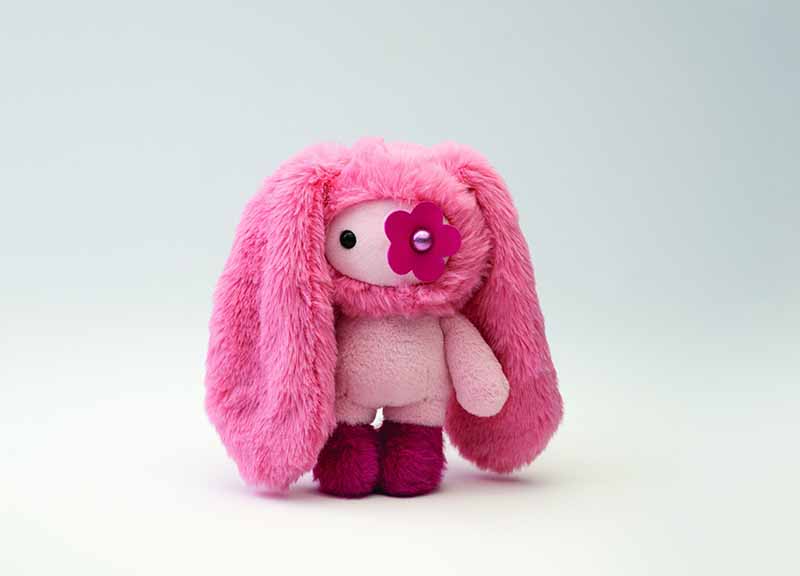 A cute pink bunny plush toy with long floppy ears and a decorative flower on its face, featuring soft fabric and playful character styling.