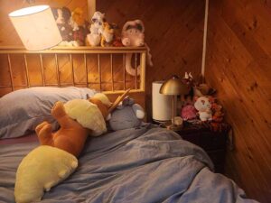 A cozy bedroom scene with several plush toys placed on the bed and shelves, creating a warm and comforting atmosphere for relaxation and sleep.