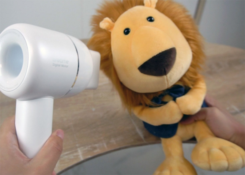 A plush lion toy being dried with a hair dryer to help restore its fluffy texture after washing or cleaning.