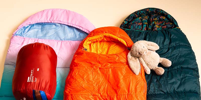 A soft plush bunny placed beside colorful sleeping bags, showing how plush toys are often used as comforting companions during sleep or travel.
