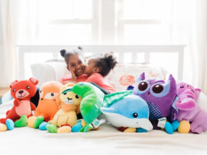 Two children sitting on a bed surrounded by colorful plush toys, showing how stuffed animals provide comfort, fun, and companionship during playtime.