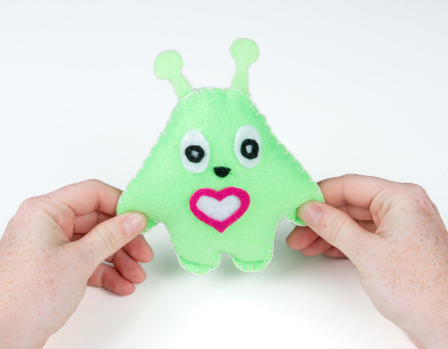 A small handmade plush toy made from felt fabric, featuring a simple character design with stitched details and a heart decoration.