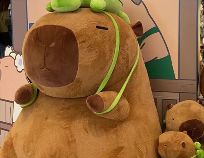 A life-size capybara plush mascot displayed at an event booth, featuring soft fabric construction and playful character styling for promotional or decorative use.