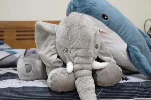 Soft elephant and shark plush toys placed on a bed, highlighting oversized design, realistic detailing, and cozy home décor appeal.