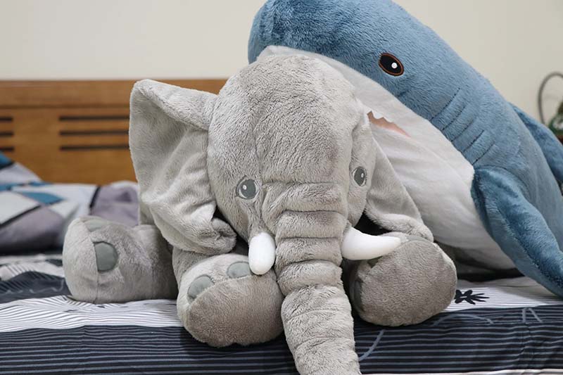 Soft elephant and shark plush toys placed on a bed, highlighting oversized design, realistic detailing, and cozy home décor appeal.