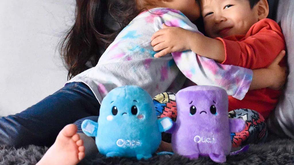 Two children hugging while small expressive plush toys sit in front, illustrating how plush toys can support emotional comfort and social interaction.