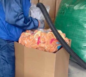 A worker uses vacuum packaging equipment to compress plush toys inside a large carton for bulk shipping and storage. The image highlights a space-saving packaging method commonly used in plush toy manufacturing to reduce shipping volume and improve transport efficiency.