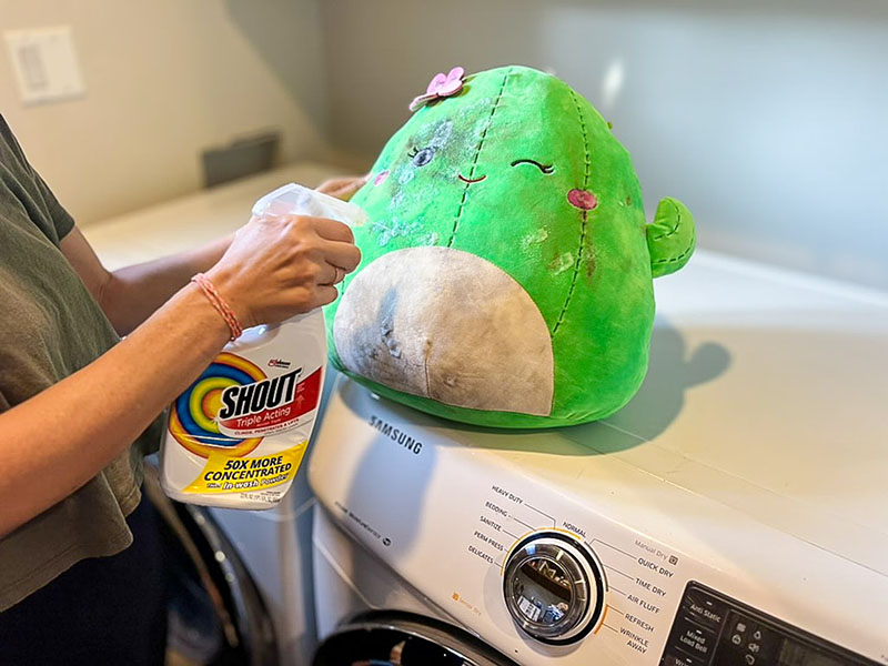 A person applying stain remover to a plush toy before washing, demonstrating how to clean and maintain stuffed animals.