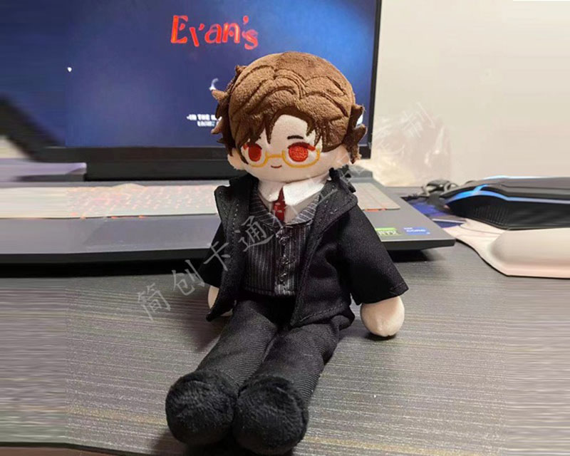 A small anime-inspired plush doll dressed in a detailed suit outfit, featuring embroidered facial details and styled fabric hair, displayed on a desk in a casual setting.