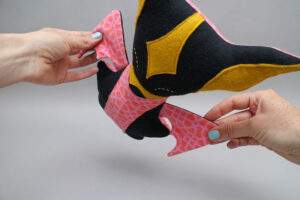 A felt bat plush toy held in hands, showing stitched details and colorful fabric panels typical of handmade plush craft design.
