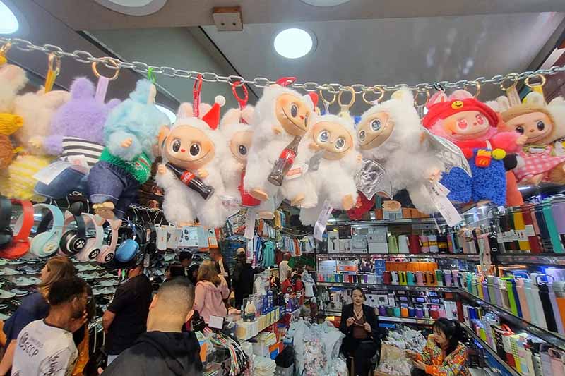 A row of plush keychain toys hanging from a chain display inside a busy retail shop, showcasing collectible character designs and gift items.