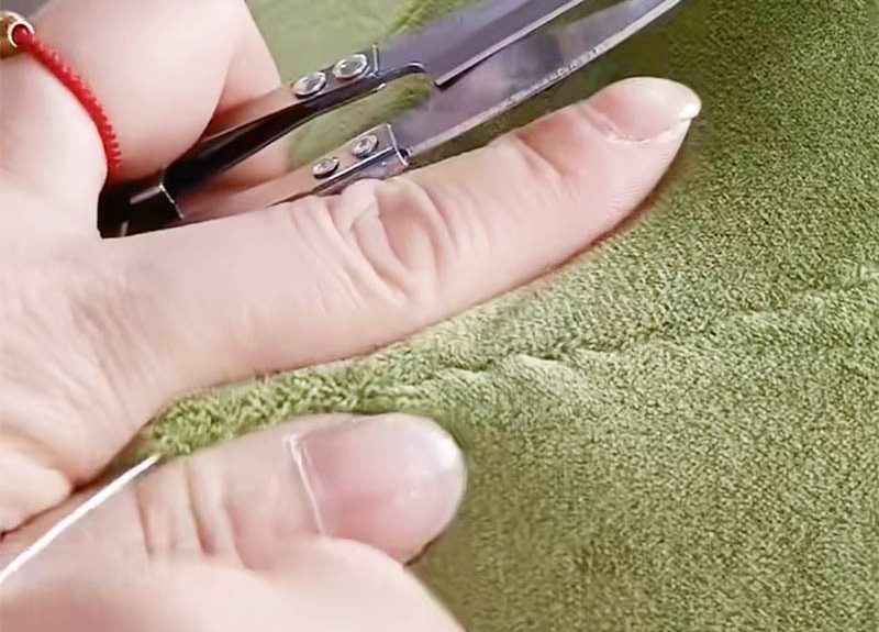 Close-up of trimming plush fabric seam using small sewing scissors