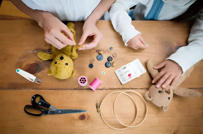 People hand-sewing plush toys with buttons, thread, and sewing tools on table