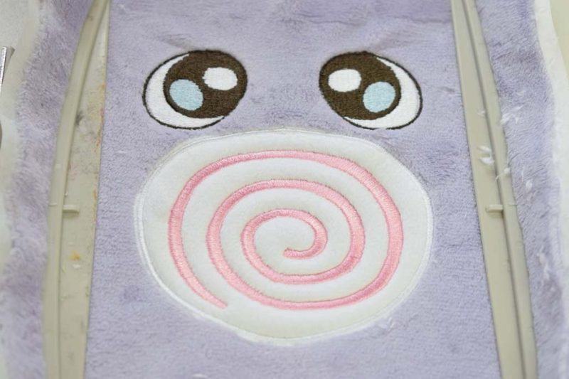 Close-up of embroidered plush toy face with spiral mouth and stitched eyes